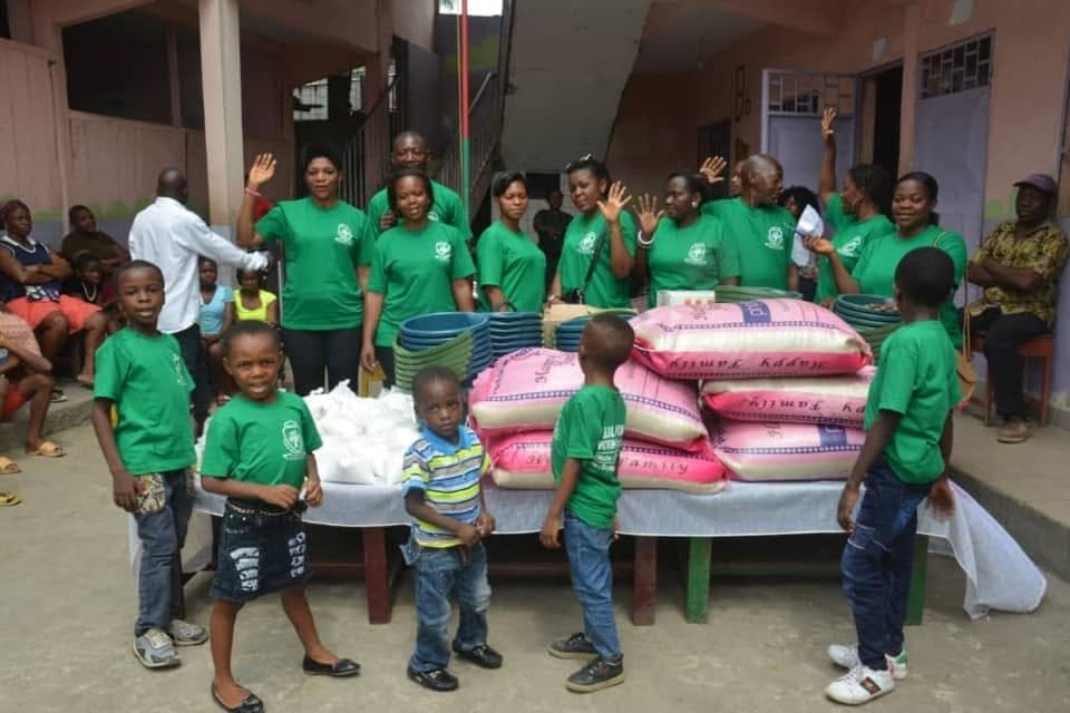 Volunteers and children gathered around bags of rice and supplies at a Be Real Humanitarian Works distribution