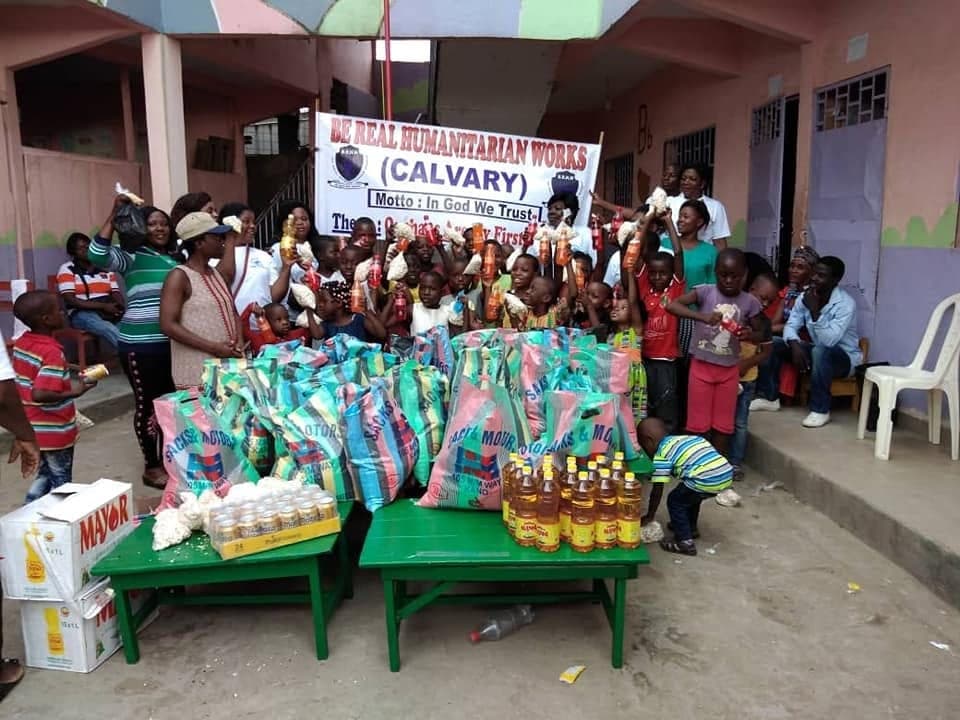 Children celebrating with volunteers around bags of rice and supplies at a Be Real Humanitarian Works distribution