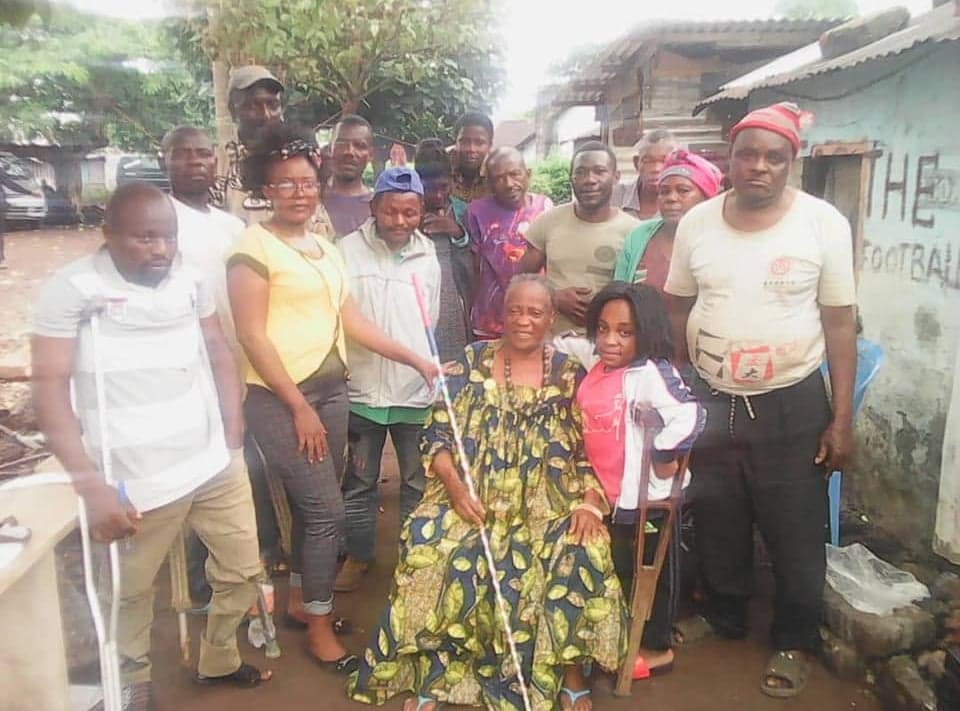 A blind elderly woman surrounded by family and community members during a Be Real Humanitarian Works visit